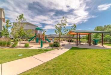 A children's playground sits next to a covered picnic area. A concrete path leads to the seating area and playground.