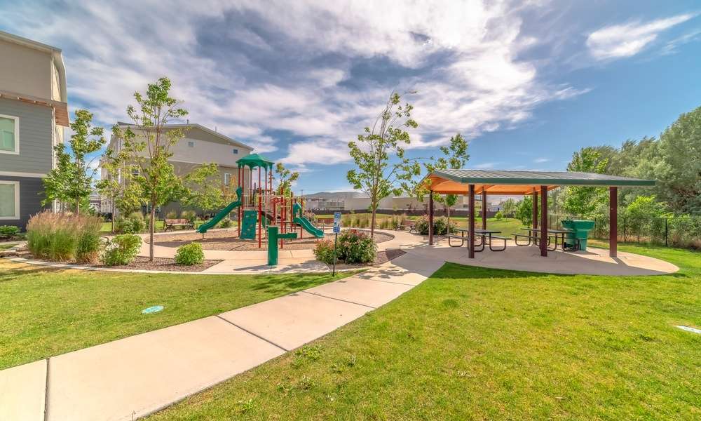 A children's playground sits next to a covered picnic area. A concrete path leads to the seating area and playground.