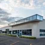 A commercial building has light gray brick walls, blue metal siding, and darkened windows. The parking lot is empty.