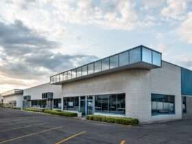 A commercial building has light gray brick walls, blue metal siding, and darkened windows. The parking lot is empty.