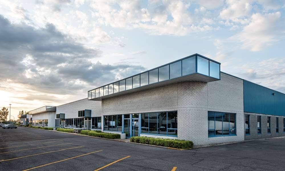 A commercial building has light gray brick walls, blue metal siding, and darkened windows. The parking lot is empty.