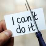 Close-up of a person's hands cutting a piece of paper reading "I can't do it." They are trimming off the "t" in "can't."