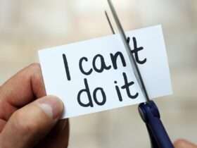 Close-up of a person's hands cutting a piece of paper reading "I can't do it." They are trimming off the "t" in "can't."