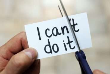 Close-up of a person's hands cutting a piece of paper reading "I can't do it." They are trimming off the "t" in "can't."