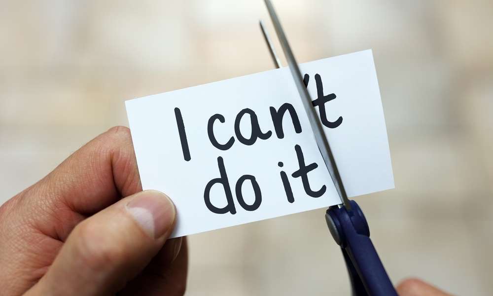 Close-up of a person's hands cutting a piece of paper reading "I can't do it." They are trimming off the "t" in "can't."