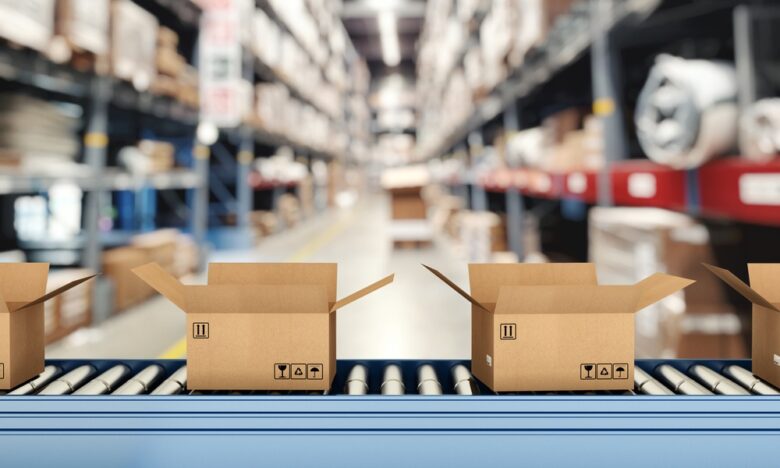 A close-up of a roller conveyor belt with multiple open cardboard boxes inside a warehouse with tall shelves.