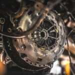 Exposed clutch assembly sits inside a vehicle undercarriage. Wires and hoses hang around the metal housing.