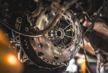 Exposed clutch assembly sits inside a vehicle undercarriage. Wires and hoses hang around the metal housing.