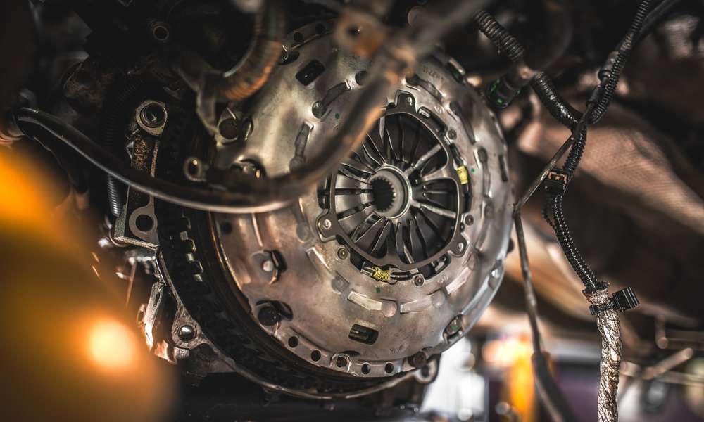 Exposed clutch assembly sits inside a vehicle undercarriage. Wires and hoses hang around the metal housing.
