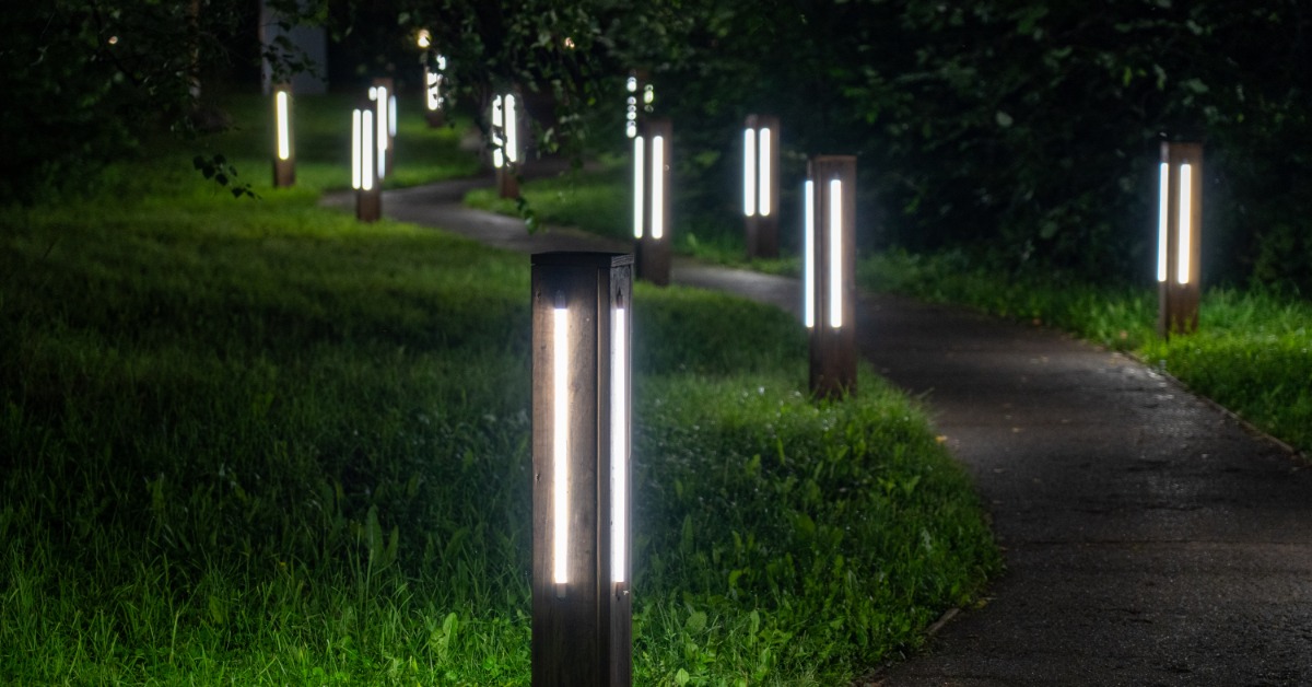 LED bollard lights illuminate a winding walkway through a park at night with grass bordering the path.