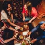 Two couples sitting together in a booth. They have several plates of food on their table while they laugh and eat.