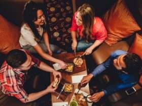 Two couples sitting together in a booth. They have several plates of food on their table while they laugh and eat.