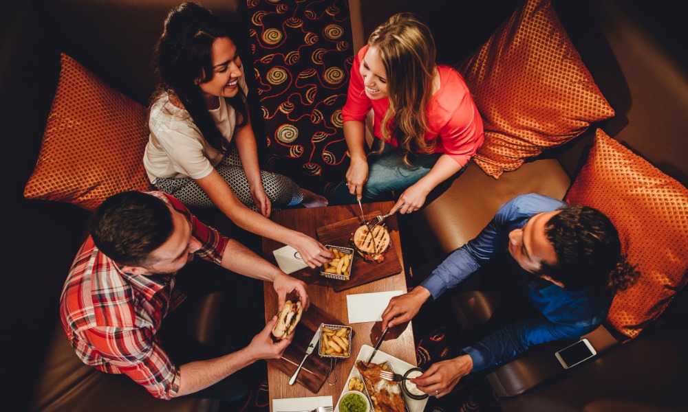 Two couples sitting together in a booth. They have several plates of food on their table while they laugh and eat.