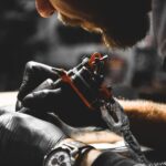 A professional tattoo artist wearing black gloves and a watch applying a tattoo to a client in their workshop.