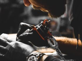 A professional tattoo artist wearing black gloves and a watch applying a tattoo to a client in their workshop.