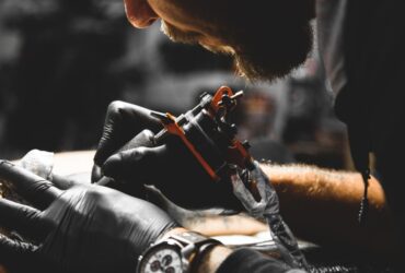 A professional tattoo artist wearing black gloves and a watch applying a tattoo to a client in their workshop.