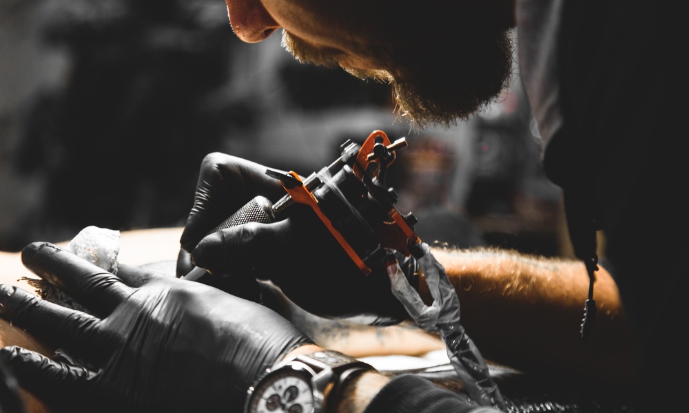 A professional tattoo artist wearing black gloves and a watch applying a tattoo to a client in their workshop.