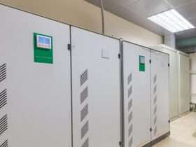 Two large industrial voltage stabilizers with digital controls installed against a white wall in a factory.