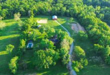 An aerial view shows a long service route linking two farmhouses, a group of storage sheds, and the surrounding acreage.