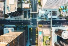 A bird's eye view of a downtown intersection that cuts through high-rise buildings, with small cars on wide streets.