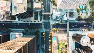 A bird's eye view of a downtown intersection that cuts through high-rise buildings, with small cars on wide streets.