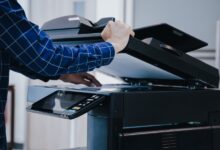 A close-up of a person adjusting a sheet of copy paper while holding the office printer's top cover open.