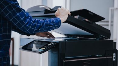 A close-up of a person adjusting a sheet of copy paper while holding the office printer's top cover open.