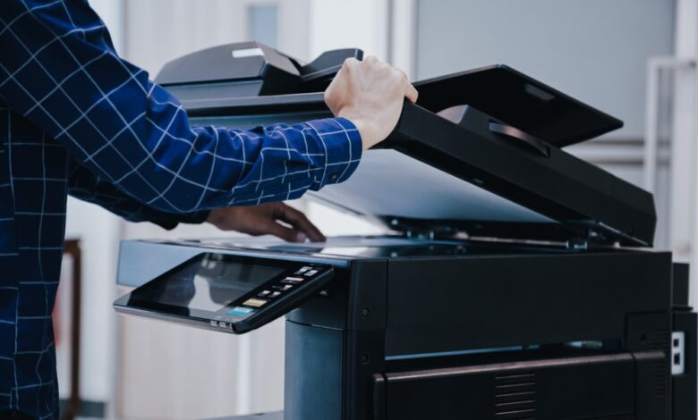 A close-up of a person adjusting a sheet of copy paper while holding the office printer's top cover open.