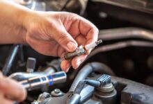 A close-up of a person using a socket tool near spark plugs and ignition coils inside an open car engine compartment.