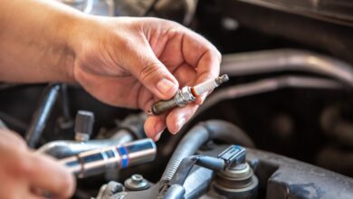 A close-up of a person using a socket tool near spark plugs and ignition coils inside an open car engine compartment.