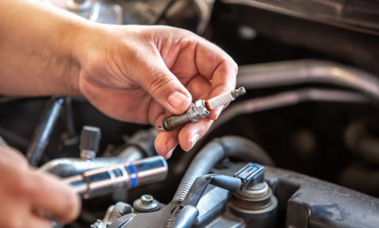 A close-up of a person using a socket tool near spark plugs and ignition coils inside an open car engine compartment.