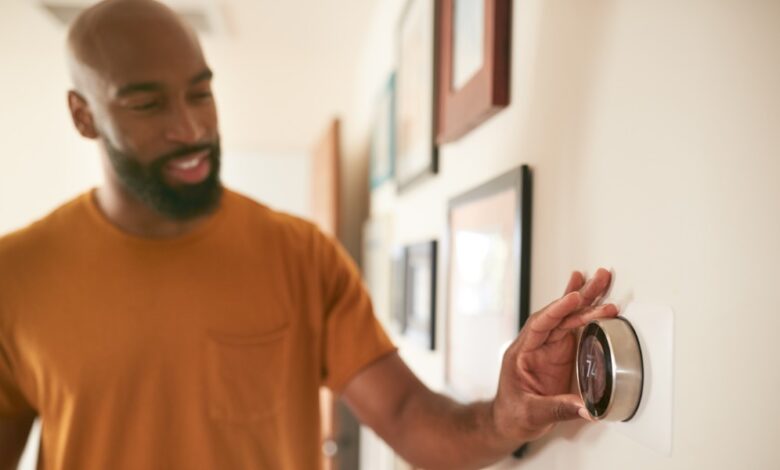 A man reaching toward a wall thermostat display near a doorway in a bright home interior with soft light.