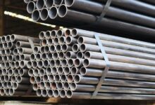 Bundles of long steel pipes are stacked and secured with metal straps inside an industrial warehouse storage area.