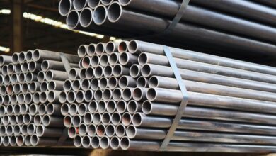 Bundles of long steel pipes are stacked and secured with metal straps inside an industrial warehouse storage area.