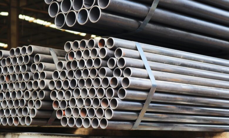 Bundles of long steel pipes are stacked and secured with metal straps inside an industrial warehouse storage area.