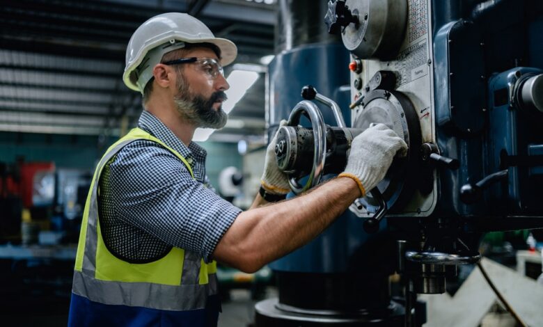 A man in a hardhat is working on a piece of industrial equipment. He’s holding a large valve and is wearing gloves.