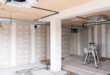 An unfinished room is under construction. There is a step ladder off to the side, and wires hang from the ceiling.