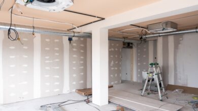 An unfinished room is under construction. There is a step ladder off to the side, and wires hang from the ceiling.