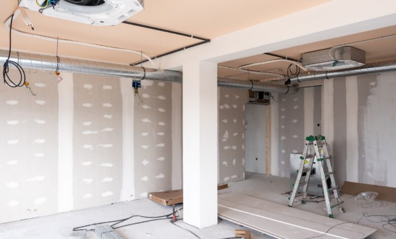 An unfinished room is under construction. There is a step ladder off to the side, and wires hang from the ceiling.