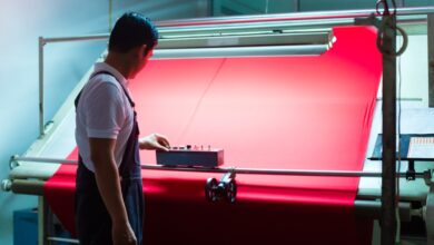A man standing in front of a machine holding a large sheet of red textile, pushing a button on a remote control.