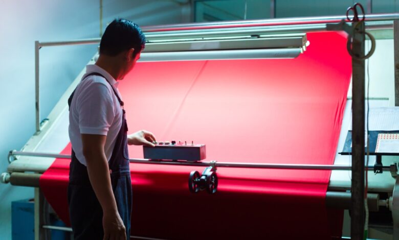 A man standing in front of a machine holding a large sheet of red textile, pushing a button on a remote control.