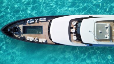 An aerial view of a large, white superyacht floating in turquoise water, with a small lounging pool in the front.