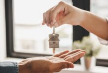 A close-up of a hand dropping a set of keys with a metal house keychain into another hand underneath in a room.