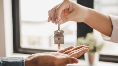 A close-up of a hand dropping a set of keys with a metal house keychain into another hand underneath in a room.