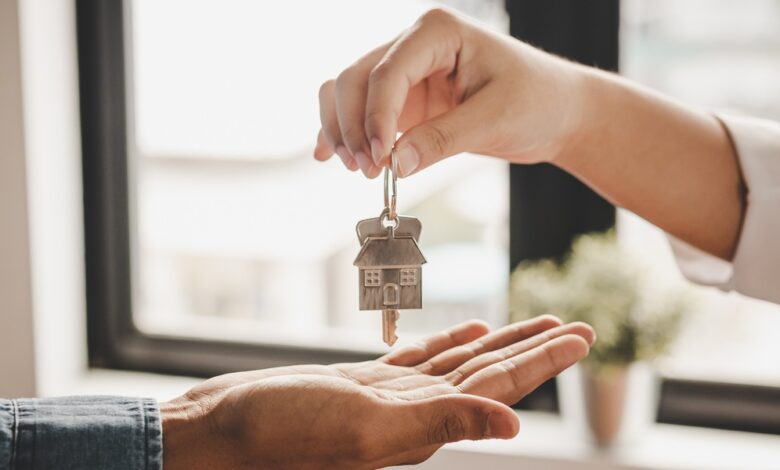 A close-up of a hand dropping a set of keys with a metal house keychain into another hand underneath in a room.