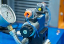A pressure gauge is attached to a solenoid valve. The solenoid valve sits on top of a blue piece of metal.