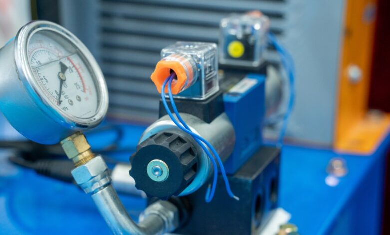 A pressure gauge is attached to a solenoid valve. The solenoid valve sits on top of a blue piece of metal.