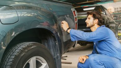 A man in a blue jumpsuit is kneeling down next to a truck. The man is in a garage environment.