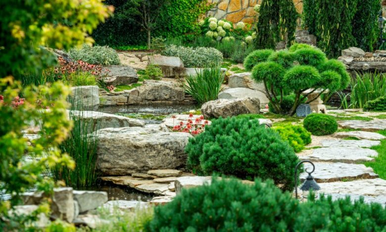 Landscaped garden with sculpted evergreens, large rocks, flowering plants, a small pond, and stone pathways.