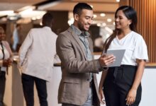 Two professionals talking at a trade show near two other employees. One of them holds a small tablet.